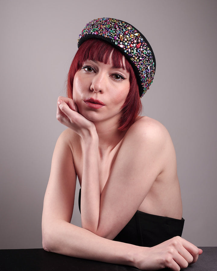 The model showcases the front of the Lumi Beret, crafted in classic black felt, and adorned with multi-coloured crystals that wrap across the front to the side of the brim. Designed by Merve Bayindir.