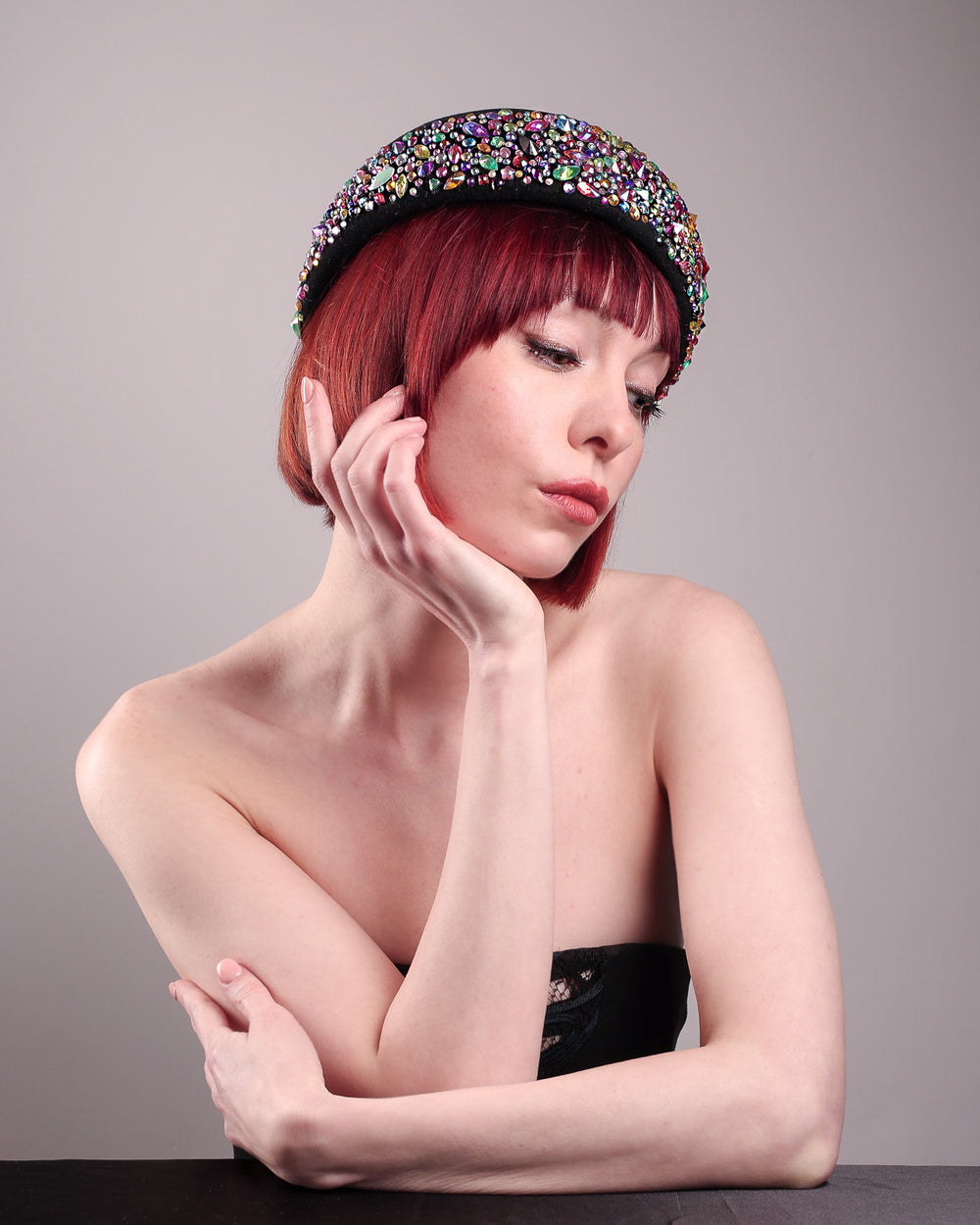 The model showcases the right side front of the Lumi Beret, crafted in classic black felt, and adorned with multi-coloured crystals that wrap across the front to the side of the brim. Designed by Merve Bayindir.