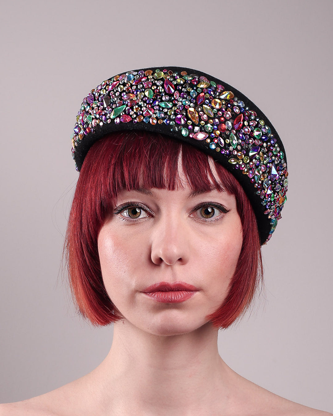 The model showcases the front close up of the Lumi Beret, crafted in classic black felt, and adorned with multi-coloured crystals that wrap across the front to the side of the brim. Designed by Merve Bayindir.