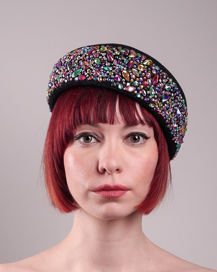 The model showcases the front close up of the Lumi Beret, crafted in classic black felt, and adorned with multi-coloured crystals that wrap across the front to the side of the brim. Designed by Merve Bayindir.