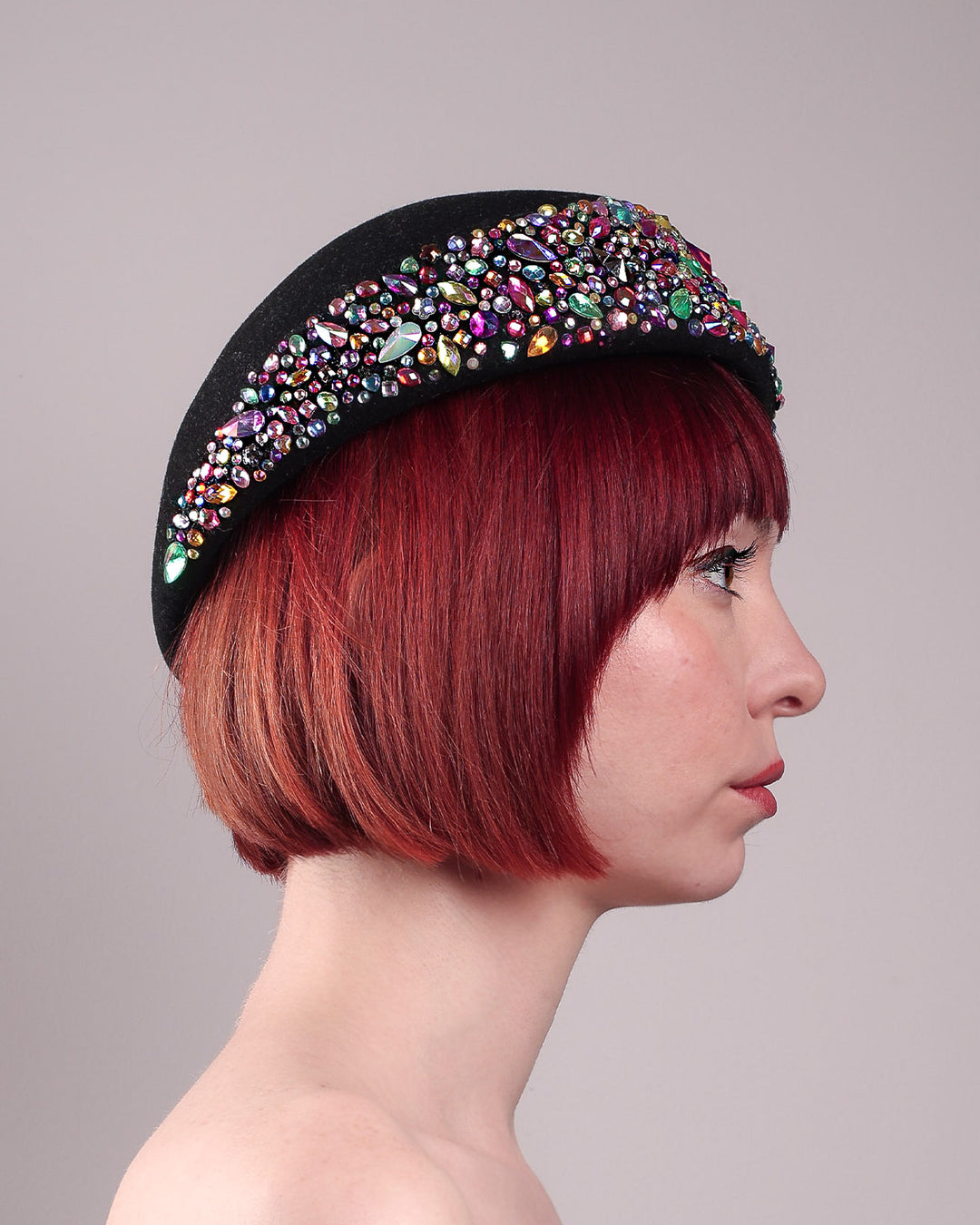 The model showcases the right side close up of the Lumi Beret, crafted in classic black felt, and adorned with multi-coloured crystals that wrap across the front to the side of the brim. Designed by Merve Bayindir.
