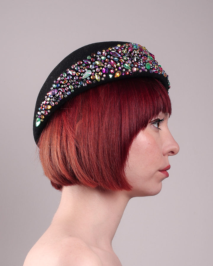 The model showcases the right side close up of the Lumi Beret, crafted in classic black felt, and adorned with multi-coloured crystals that wrap across the front to the side of the brim. Designed by Merve Bayindir.