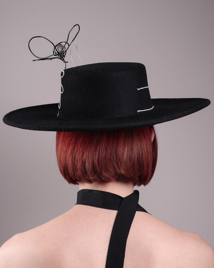 The model showcases the back of the Lune wide-brim boater hat, crafted in deep black felt, the hat&