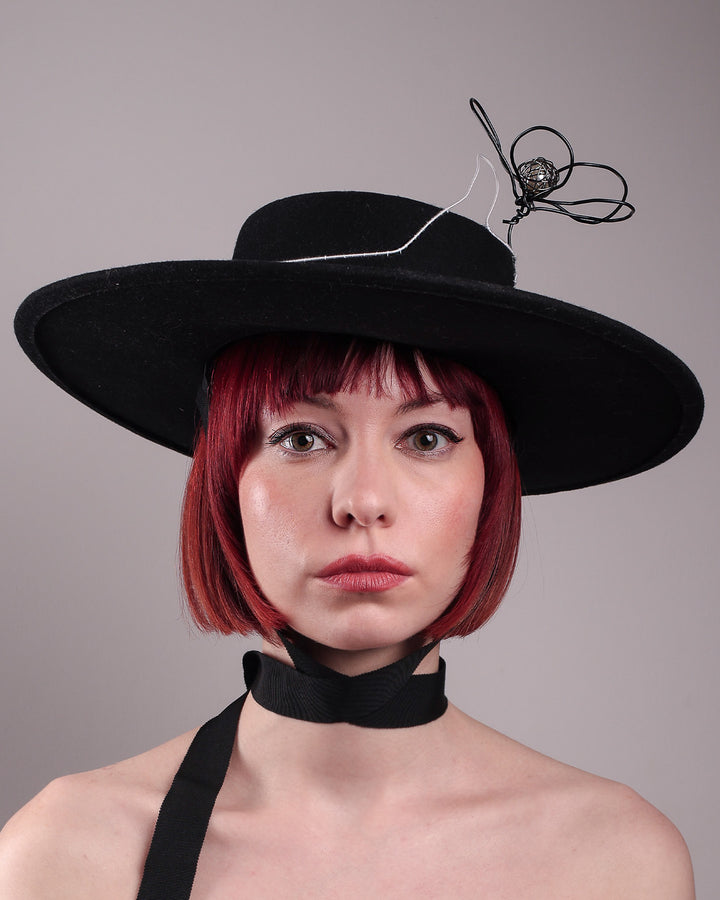 The model showcases the front close up of the Lune wide-brim boater hat, crafted in deep black felt, the hat&