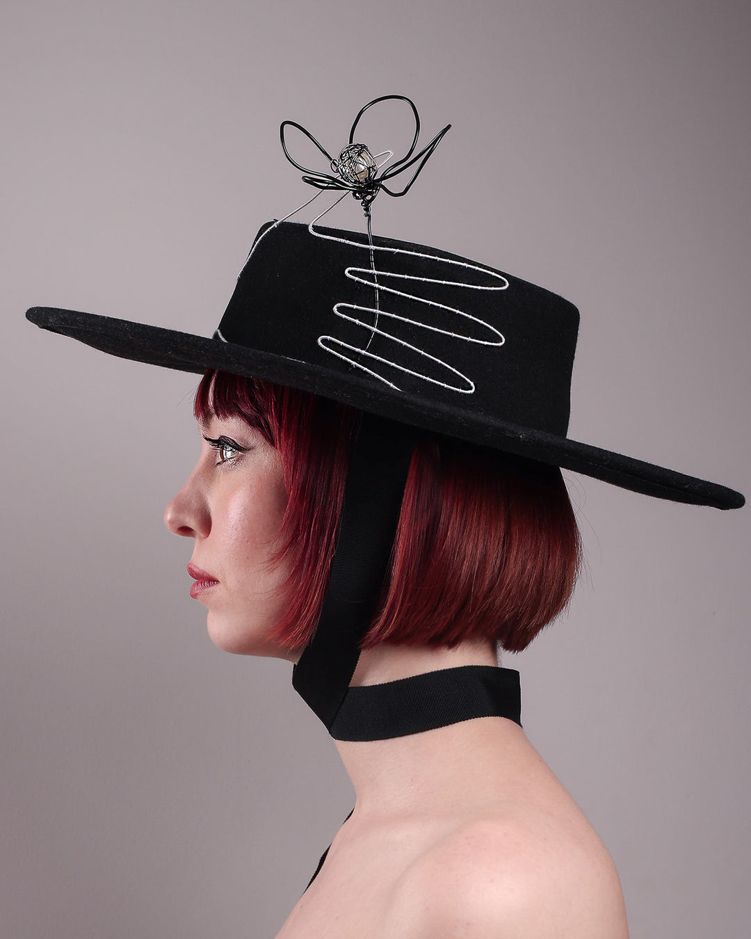 The model showcases the left side close up of the Lune wide-brim boater hat, crafted in deep black felt, the hat&