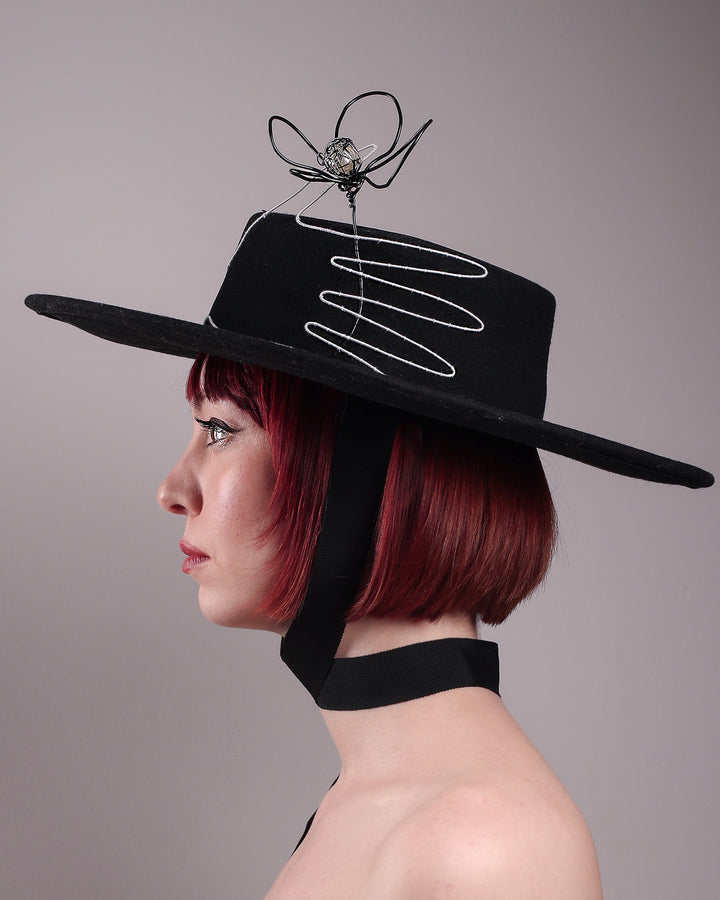 The model showcases the left side close up of the Lune wide-brim boater hat, crafted in deep black felt, the hat&