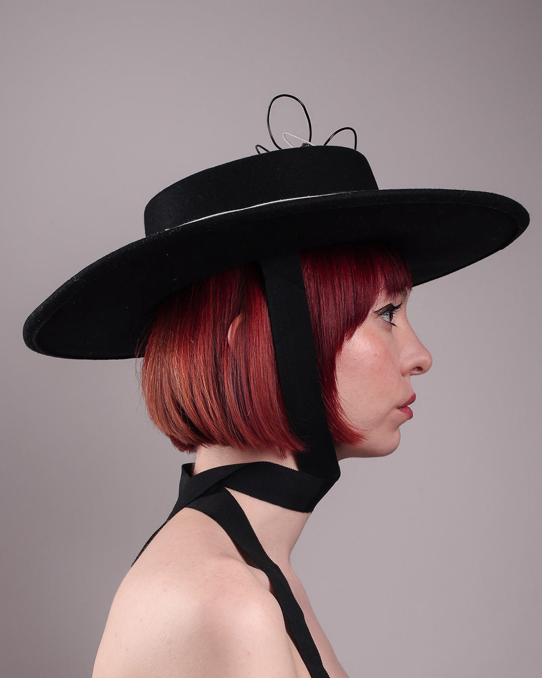 The model showcases the right side close up of the Lune wide-brim boater hat, crafted in deep black felt, the hat&