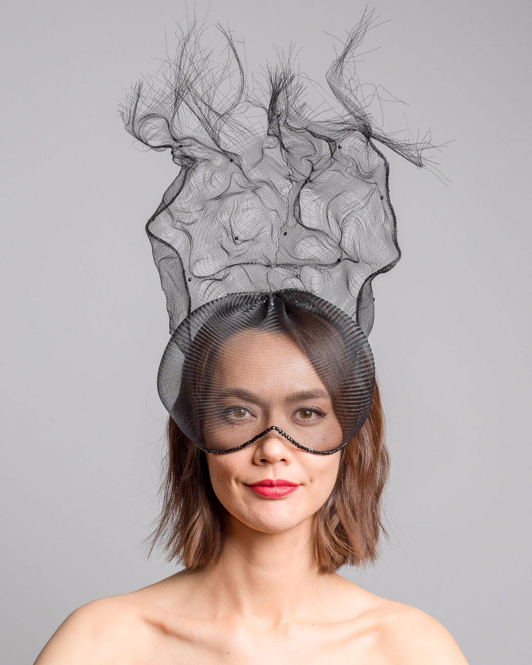 The model is showcasing the front side close up of the half mesh mask with extension the the teared crinoline to the back decorated with Original Crystals rhinestones. Designed and made by Merve Bayindir Millinery.