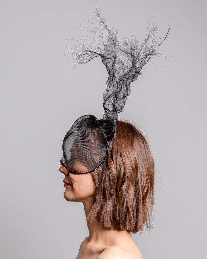 The model is showcasing the left  side close up of the half mesh mask with extension the the teared crinoline to the back decorated with Original Crystals rhinestones. Designed and made by Merve Bayindir Millinery.