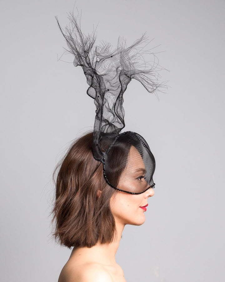 The model is showcasing the right side close up of the half mesh mask with extension the the teared crinoline to the back decorated with Original Crystals rhinestones. Designed and made by Merve Bayindir Millinery.