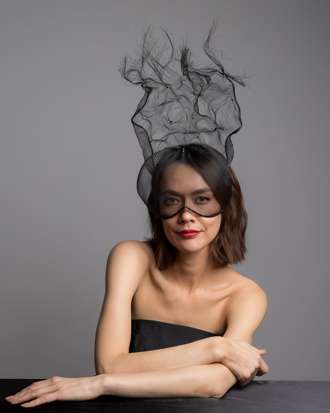 The female model is posing, wearing
Mora, the half mesh mask with extension the the teared crinoline to the back decorated with Original Crystals rhinestones. Designed and made by Merve Bayindir Millinery.