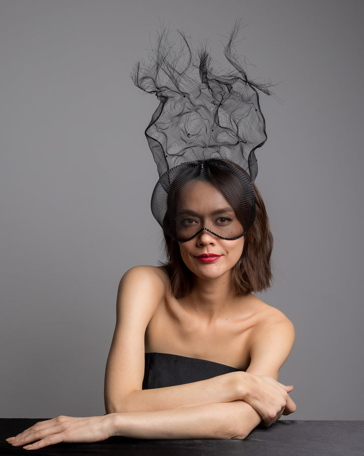 The female model is posing, wearing
Mora, the half mesh mask with extension the the teared crinoline to the back decorated with Original Crystals rhinestones. Designed and made by Merve Bayindir Millinery.