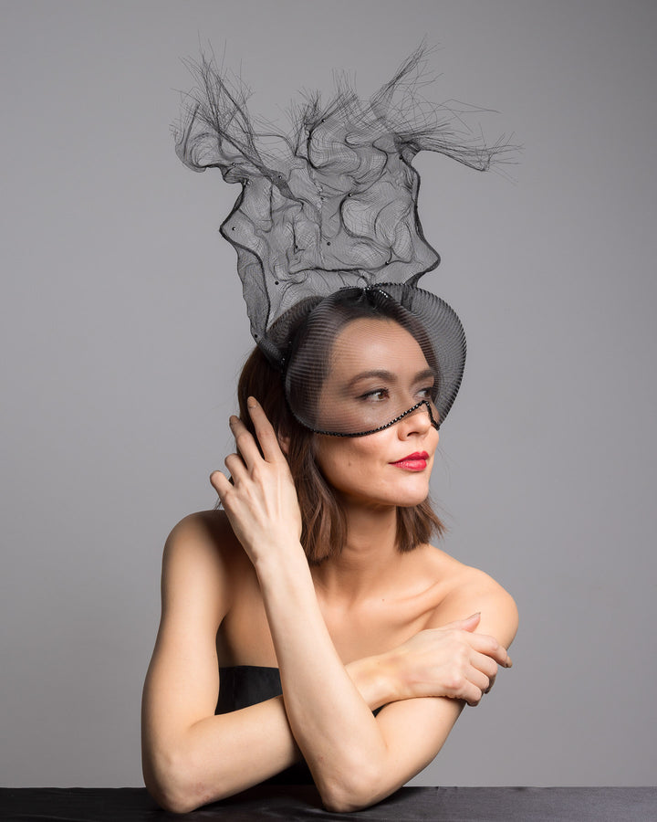 The female model is posing, wearing
Mora, the half mesh mask with extension the the teared crinoline to the back decorated with Original Crystals rhinestones. Designed and made by Merve Bayindir Millinery.