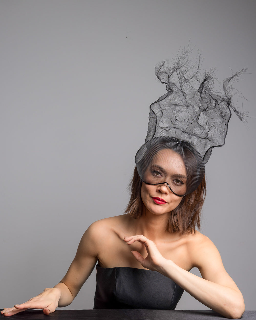 The female model is posing, wearing
Mora, the half mesh mask with extension the the teared crinoline to the back decorated with Original Crystals rhinestones. Designed and made by Merve Bayindir Millinery.
