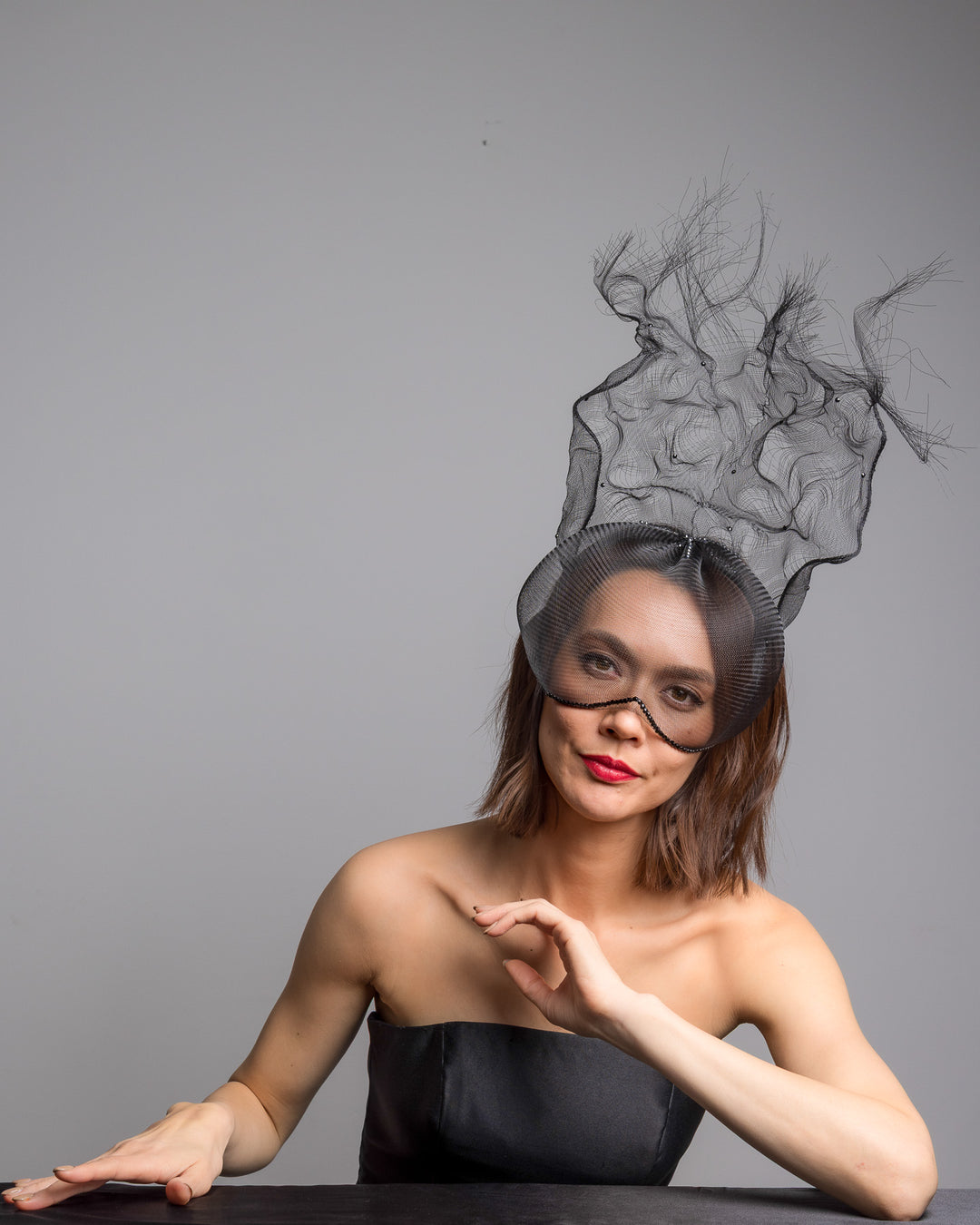 The female model is posing, wearing
Mora, the half mesh mask with extension the the teared crinoline to the back decorated with Original Crystals rhinestones. Designed and made by Merve Bayindir Millinery.