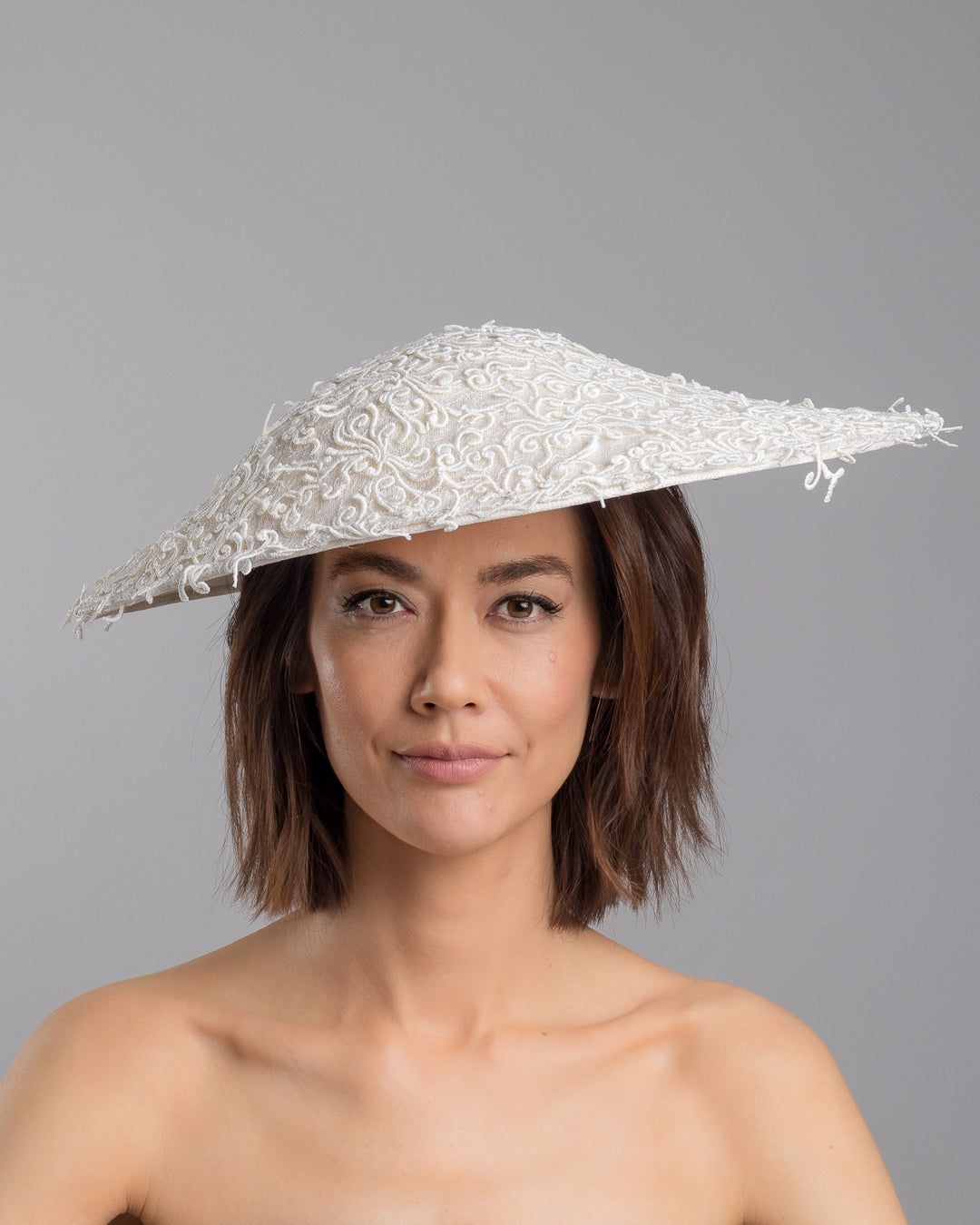 Model is showcasing the front side close up of white coloured wide brim white hat embellished with lace swirls. Designed and Made by Merve Bayindir Millinery.