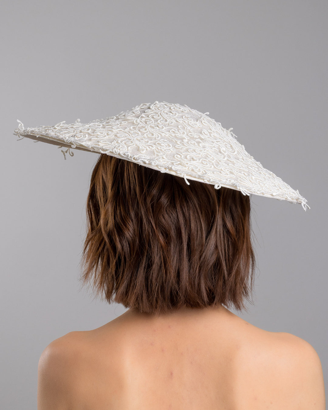 Model is showcasing the back side close up of white coloured wide brim white hat embellished with lace swirls. Designed and Made by Merve Bayindir Millinery.
