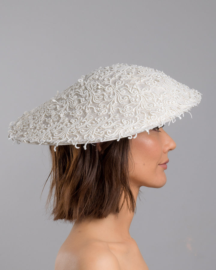 Model is showcasing the right side close up of white coloured wide brim white hat embellished with lace swirls. Designed and Made by Merve Bayindir Millinery.