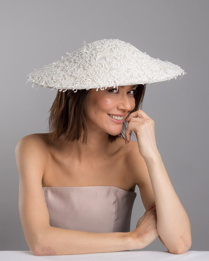 Female  model posing wearing Maribel white coloured wide brim white hat embellished with lace swirls. Designed and Made by Merve Bayindir Millinery.