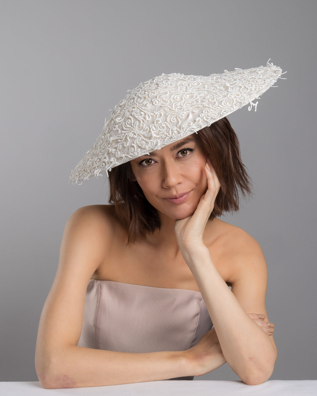 Female  model posing wearing Maribel white coloured wide brim white hat embellished with lace swirls. Designed and Made by Merve Bayindir Millinery.
