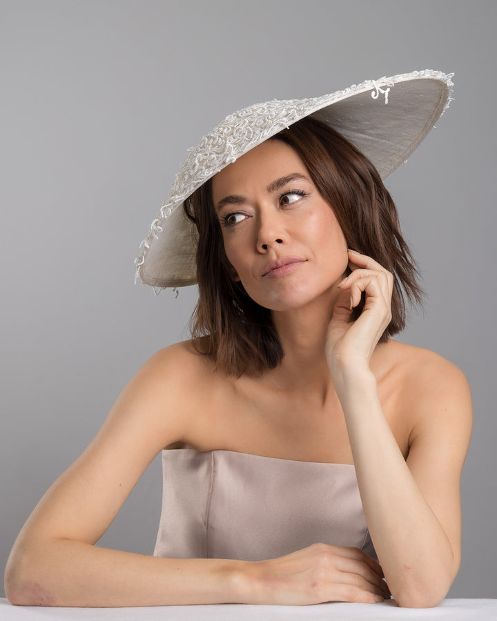 Female  model posing wearing Maribel white coloured wide brim white hat embellished with lace swirls. Designed and Made by Merve Bayindir Millinery.