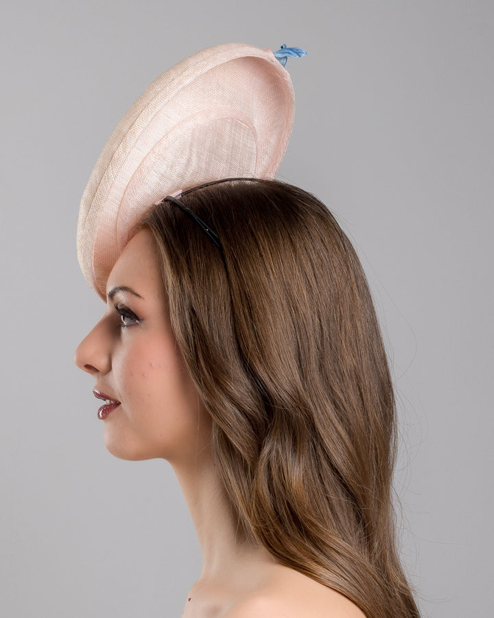 The model is showcasing the left side close up of the light pink oval high based fascinator decorated with custom made pink and blue shaded flowers. Designed and made by Merve Bayindir Millinery.
