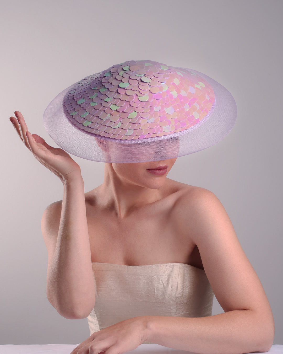 Model is showcasing the front top view of a circle shaped lilac saucer hat extended with crinoline mesh, fully embroideried with lilac and green sequins.