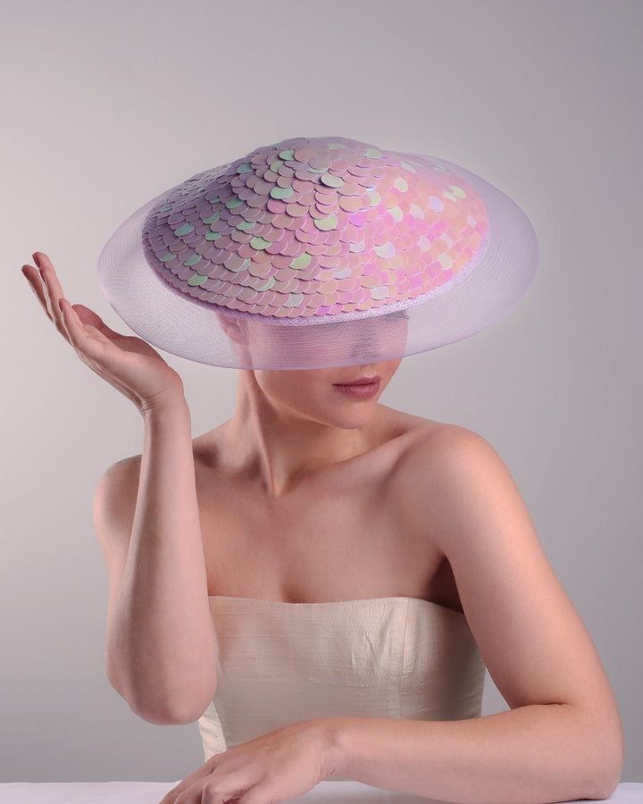 Model is showcasing the front top view of a circle shaped lilac saucer hat extended with crinoline mesh, fully embroideried with lilac and green sequins.