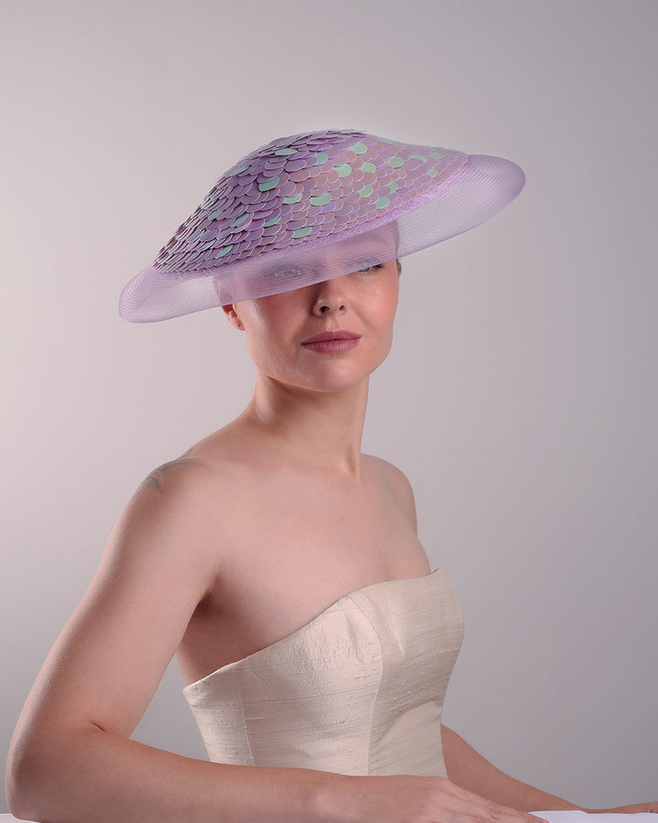 Model is showcasing the front view of a circle shaped lilac saucer hat extended with crinoline mesh, fully embroideried with lilac and green sequins.