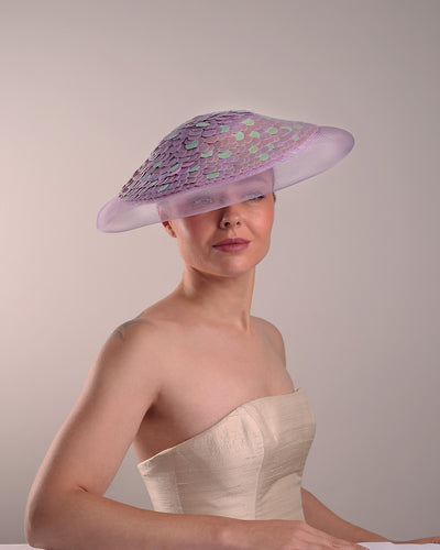 Model is showcasing the front view of a circle shaped lilac saucer hat extended with crinoline mesh, fully embroideried with lilac and green sequins.