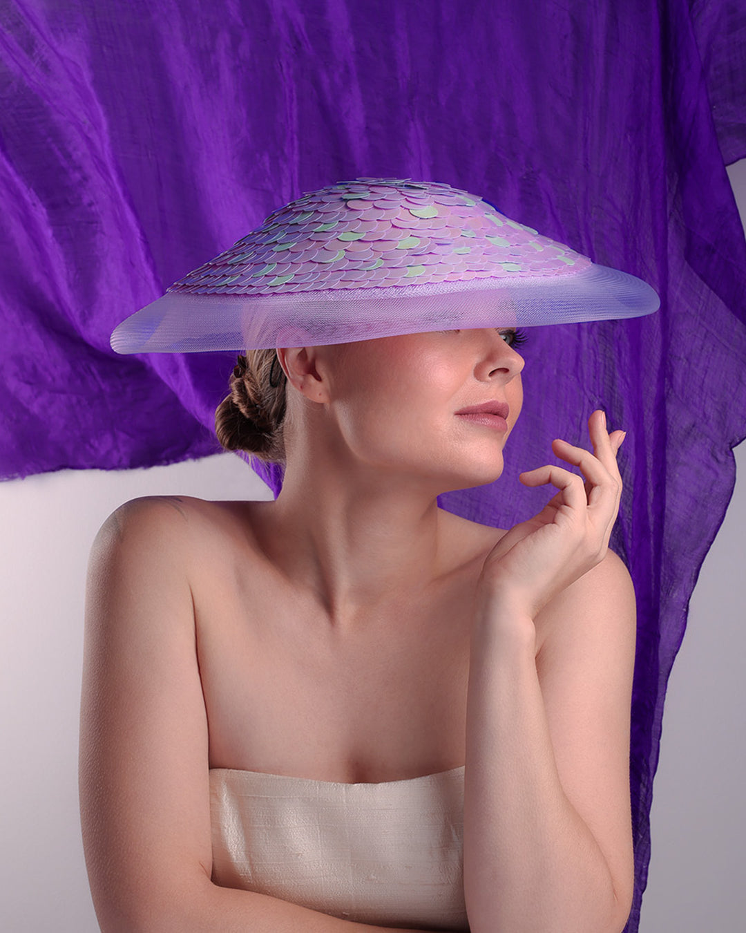 Woman wearing a large, colorful hat against a purple curtain.