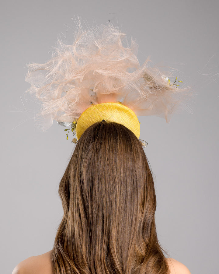 Model is showcasing the back of the double button yellow fascinator decorated with multi colour  wired resin flowers and peach crinoline clouds. Made by Merve Bayindir Millinery.