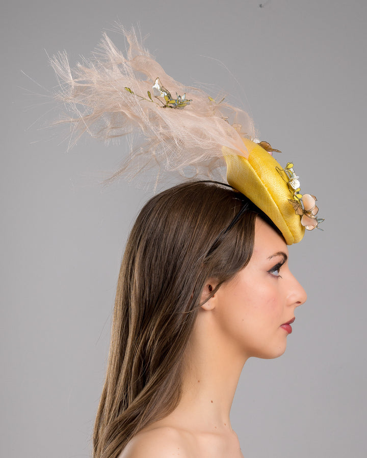 Model is showcasing the right side of the double button yellow fascinator decorated with multi colour  wired resin flowers and peach crinoline clouds. Made by Merve Bayindir Millinery.