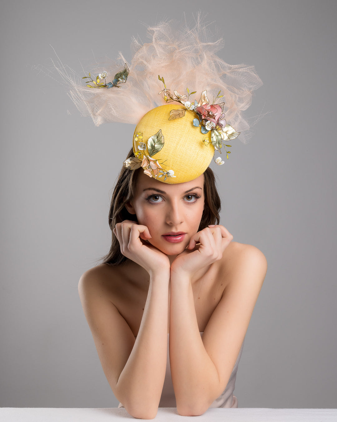 Model is posing with Merve Bayindir double button yellow fascinator decorated with multi colour  wired resin flowers and peach crinoline clouds. Made by Merve Bayindir Millinery.