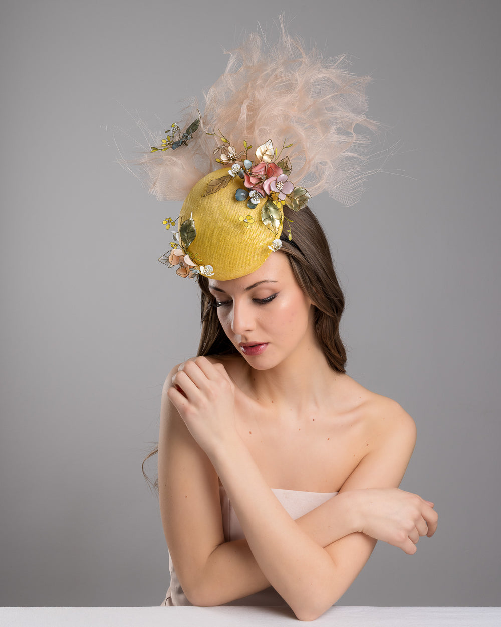 Model is posing with Merve Bayindir double button yellow fascinator decorated with multi colour  wired resin flowers and peach crinoline clouds. Made by Merve Bayindir Millinery.
