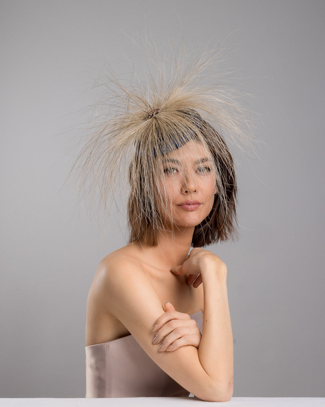 Model is posing wearing Vernum Navy coloured button shaped fascinator decorated with natural coloured burnt extra long peacock feathers and cluster of crystals. Made by Merve Baindir millinery.