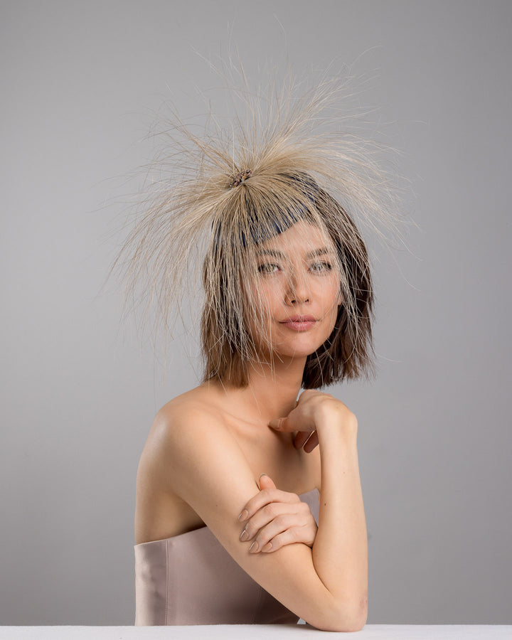 Model is posing wearing Vernum Navy coloured button shaped fascinator decorated with natural coloured burnt extra long peacock feathers and cluster of crystals. Made by Merve Baindir millinery.