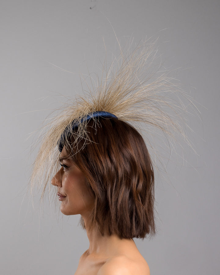 Model is showcasing the left side of Navy coloured button shaped fascinator decorated with natural coloured burnt extra long peacock feathers and cluster of crystals. Made by Merve Baindir millinery.