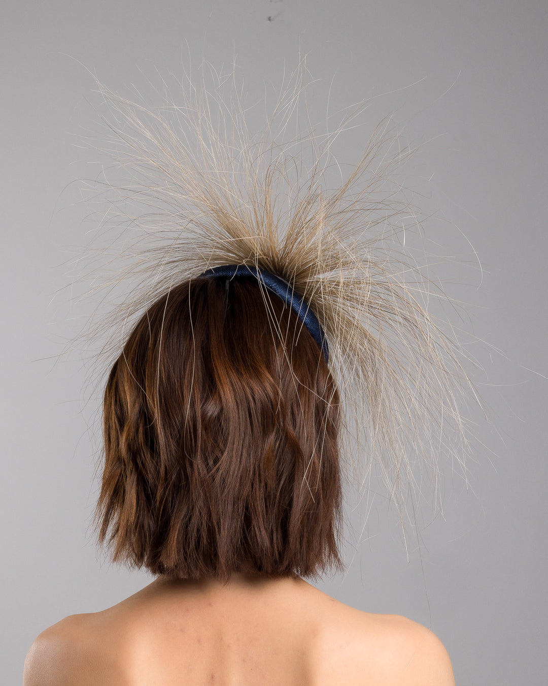 Model is showcasing the back of Navy coloured button shaped fascinator decorated with natural coloured burnt extra long peacock feathers and cluster of crystals. Made by Merve Baindir millinery.