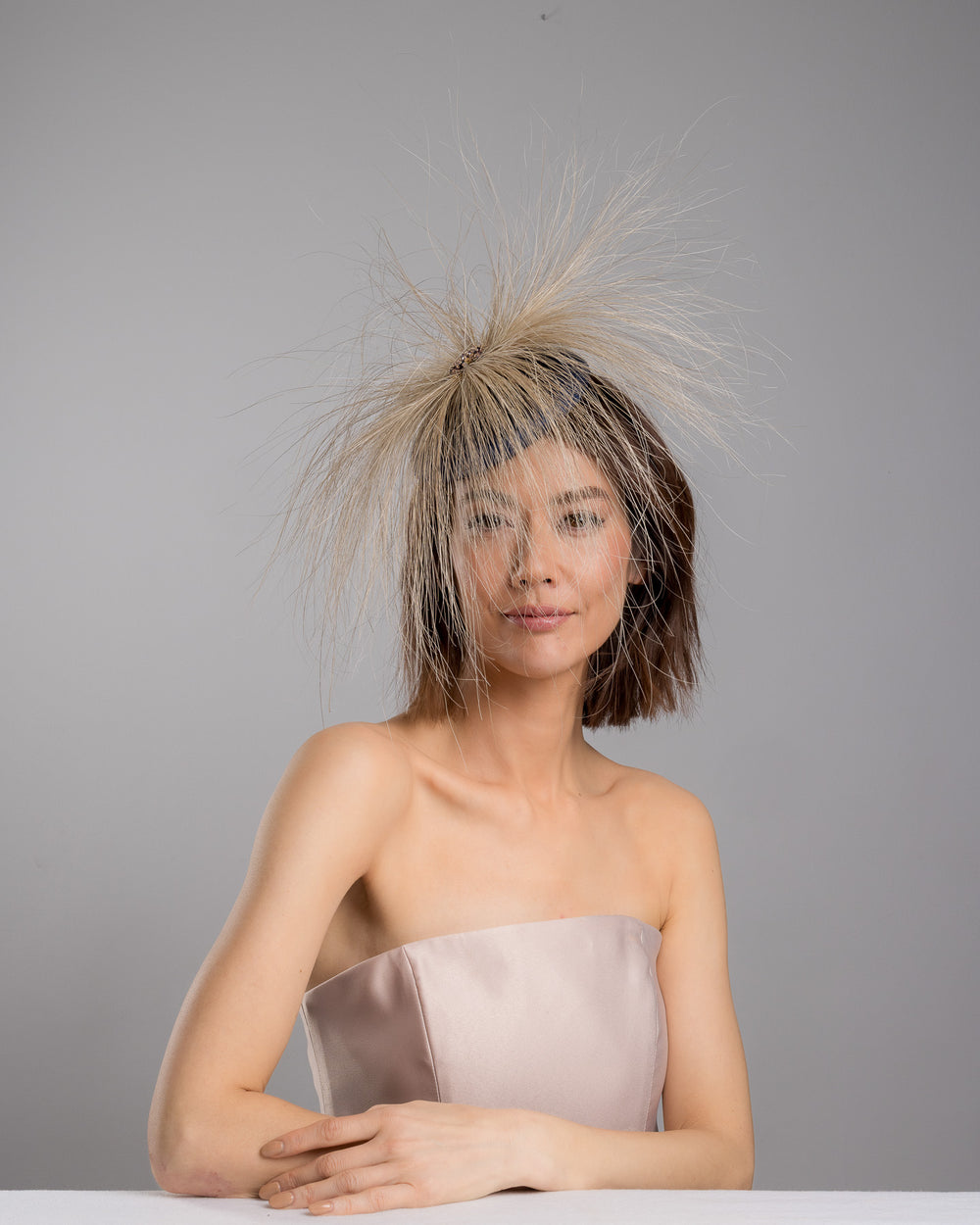 Model is posing wearing Vernum Navy coloured button shaped fascinator decorated with natural coloured burnt extra long peacock feathers and cluster of crystals. Made by Merve Baindir millinery.