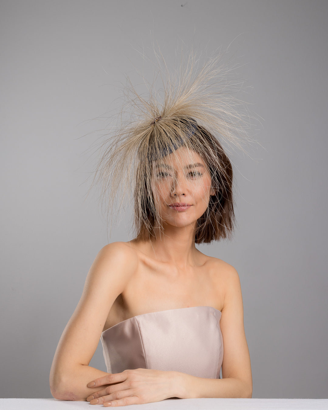 Model is posing wearing Vernum Navy coloured button shaped fascinator decorated with natural coloured burnt extra long peacock feathers and cluster of crystals. Made by Merve Baindir millinery.