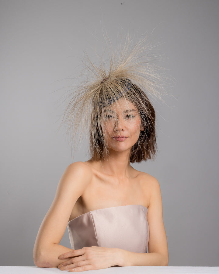 Model is posing wearing Vernum Navy coloured button shaped fascinator decorated with natural coloured burnt extra long peacock feathers and cluster of crystals. Made by Merve Baindir millinery.