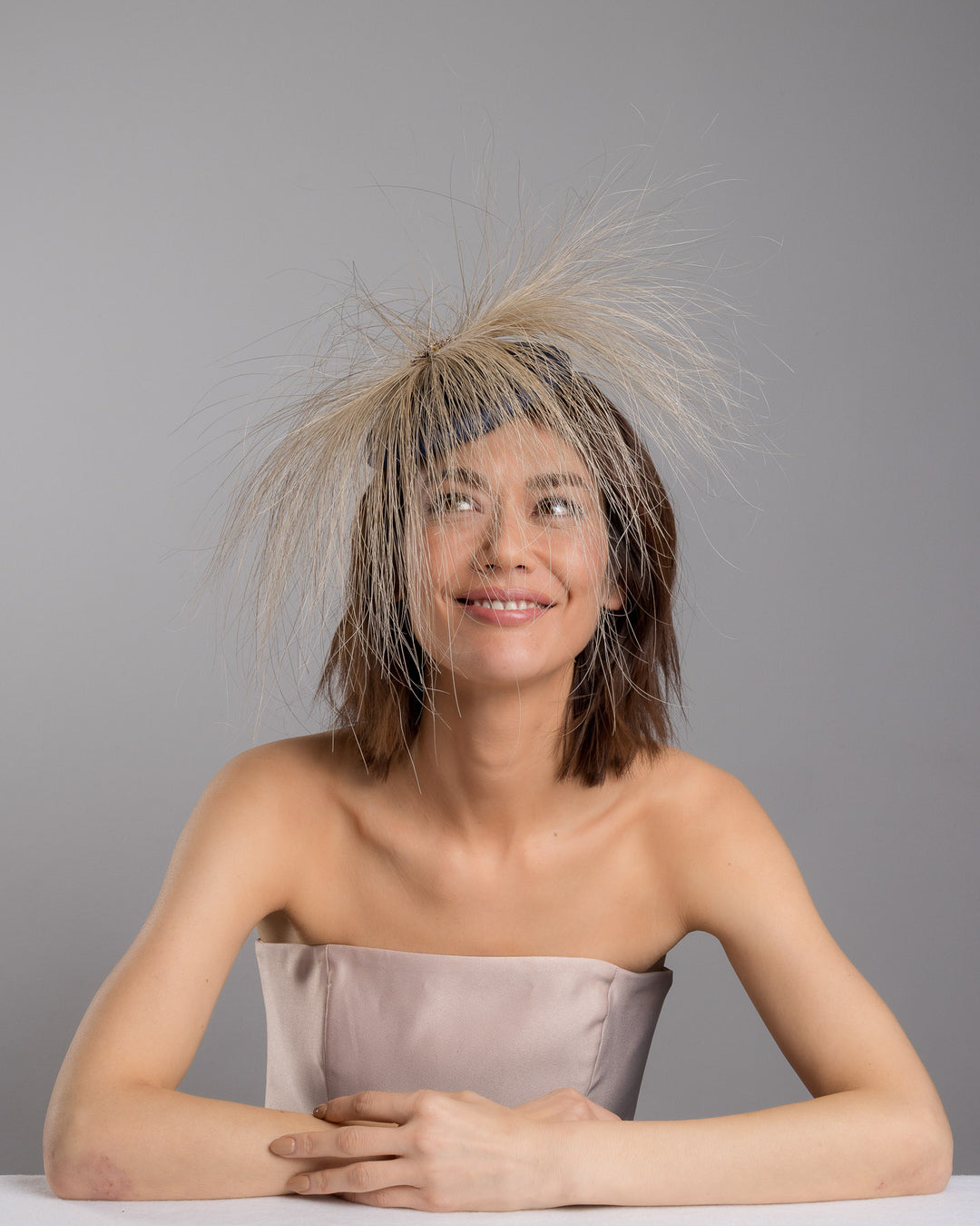 Model is posing wearing Vernum Navy coloured button shaped fascinator decorated with natural coloured burnt extra long peacock feathers and cluster of crystals. Made by Merve Baindir millinery.