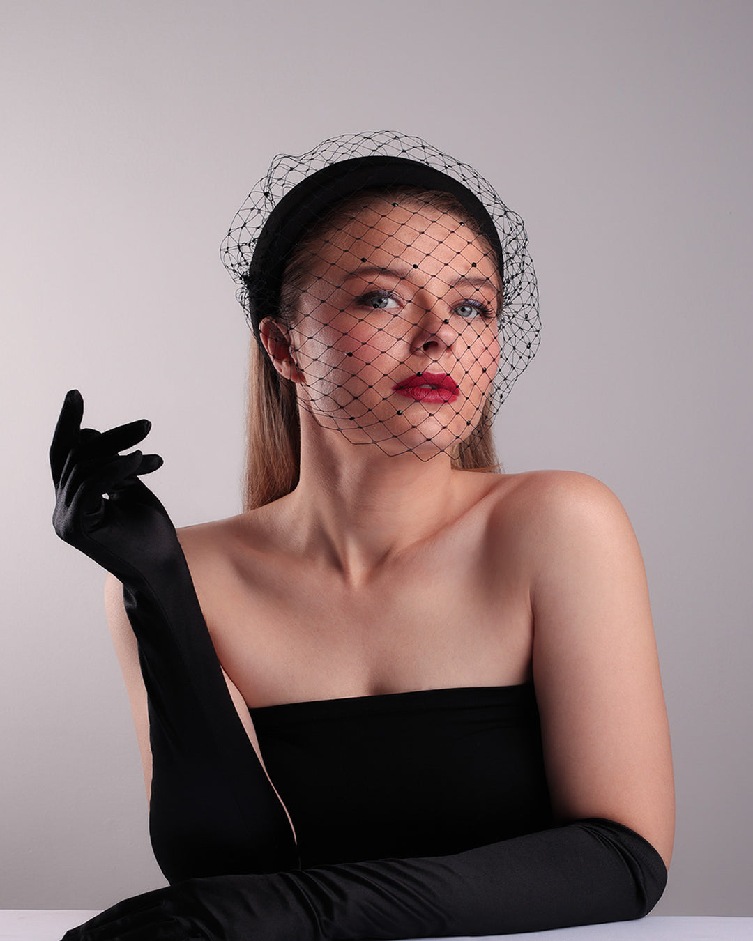 Model is showcasing the front below angle of a black high headband embellished with a black veil, adorned with black crystals.