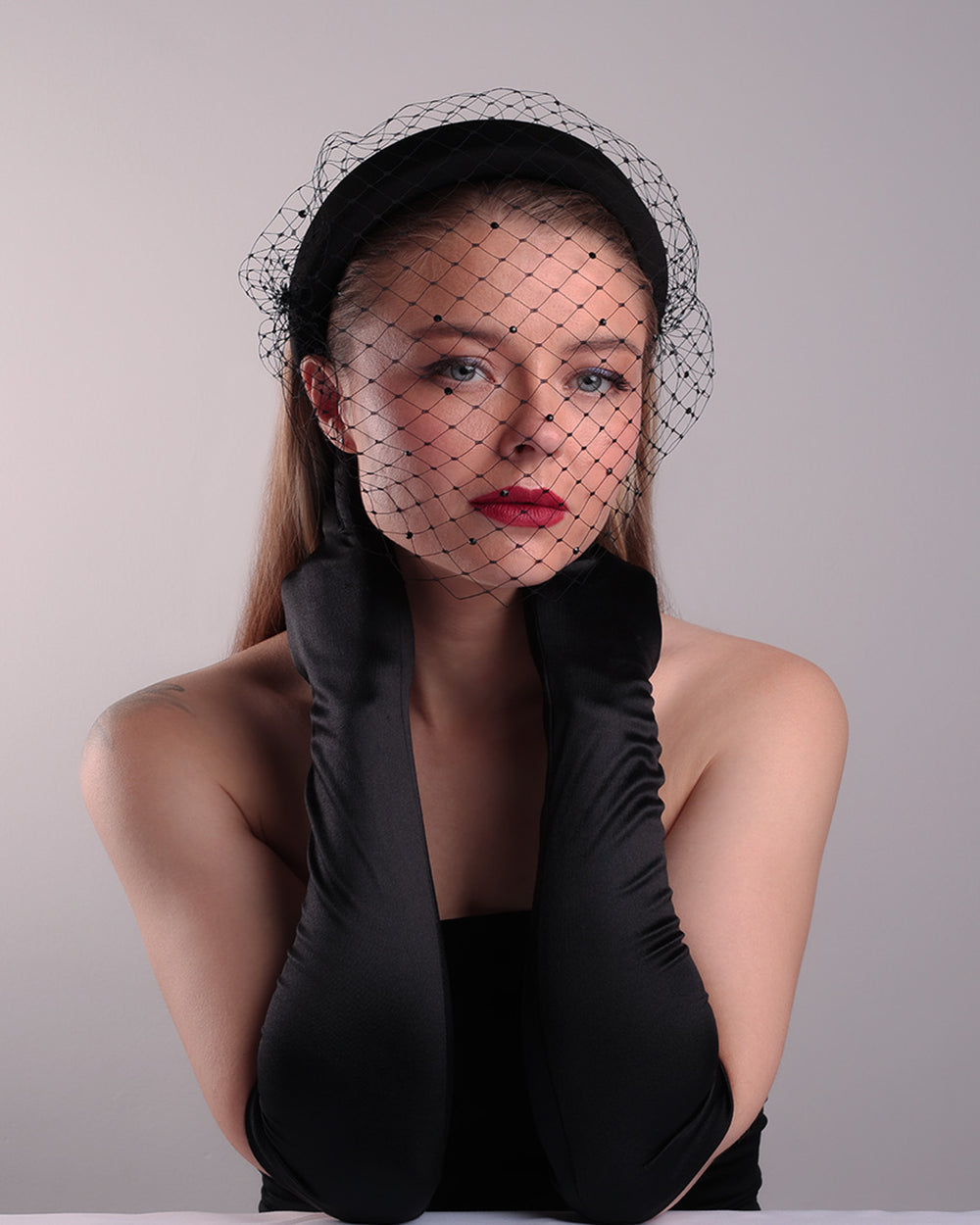 Model is showcasing the front of a black high headband embellished with a black veil, adorned with black crystals.