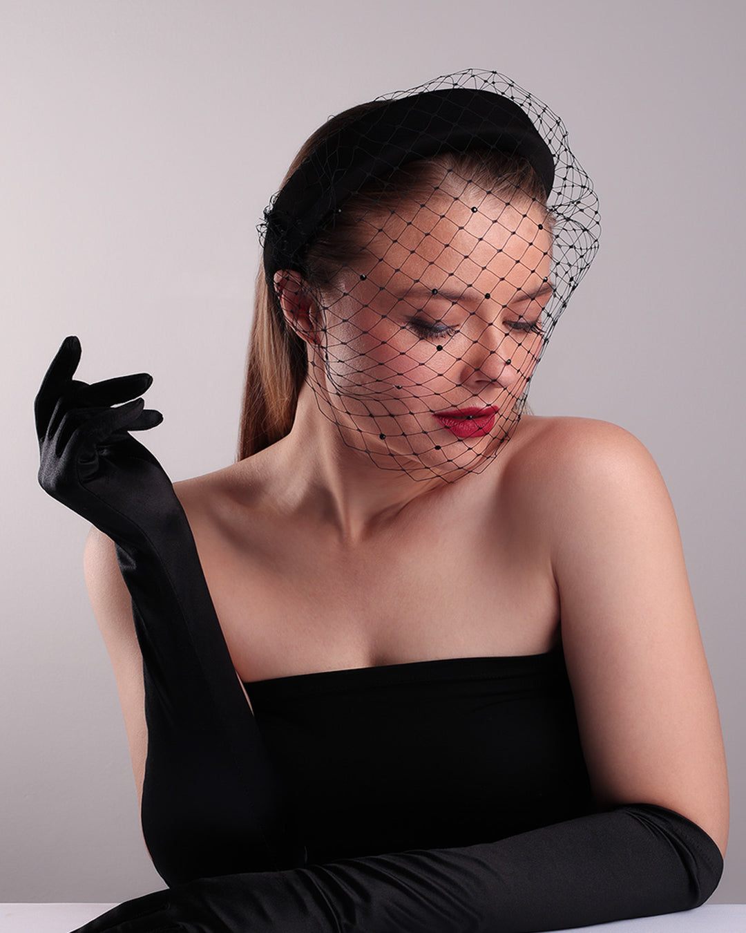 Model is showcasing the top right side of a black high headband embellished with a black veil, adorned with black crystals.