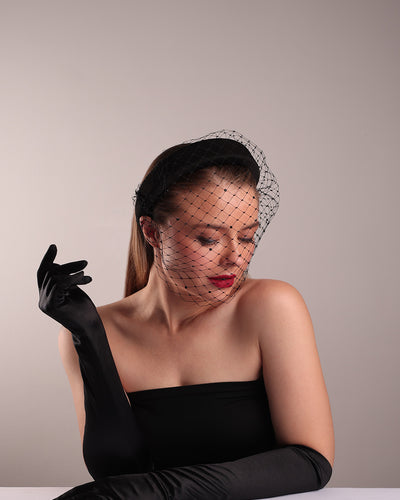 Model is showcasing the top right side of a black high headband embellished with a black veil, adorned with black crystals.