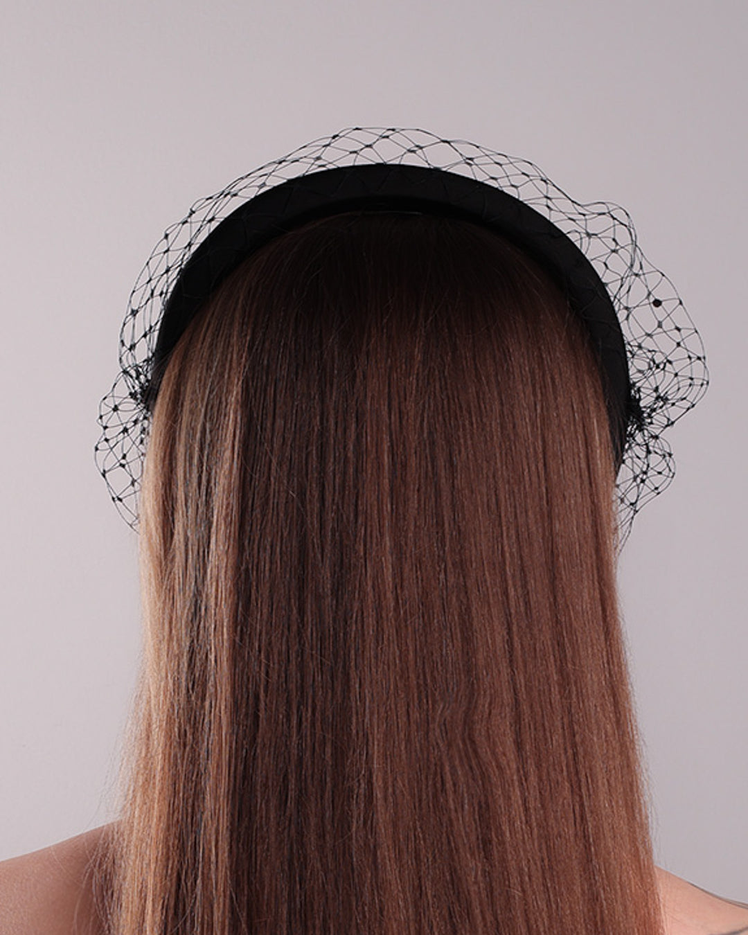 Model is showcasing the back side of a black high headband embellished with a black veil, adorned with black crystals.