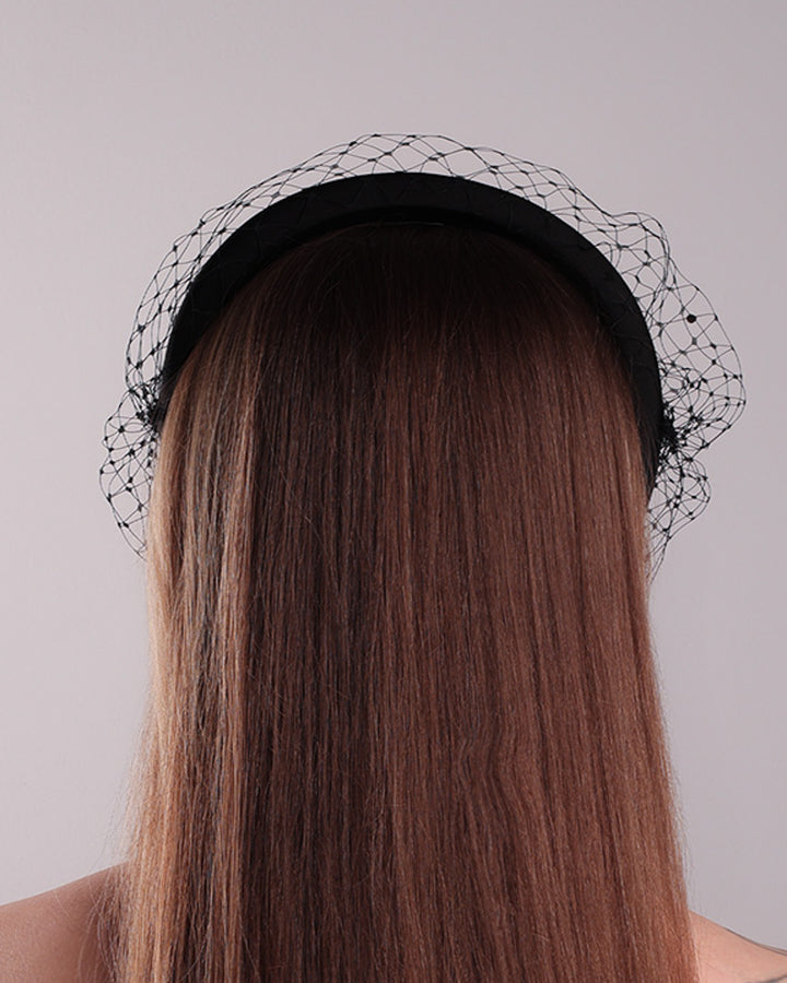 Model is showcasing the back side of a black high headband embellished with a black veil, adorned with black crystals.