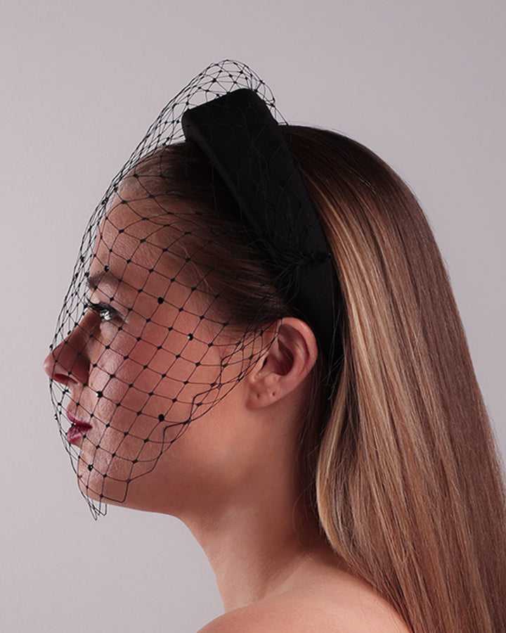 Model is showcasing the left side of a black high headband embellished with a black veil, adorned with black crystals.